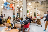 In the foreground, 3 Googlers sit together at a coffee table collaborating. Other Googlers walk in the background or the large lobby space.