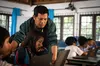 Un profesor que viste una sudadera verde se encuentra junto a una alumna frente a su Chromebook y señala la pantalla.