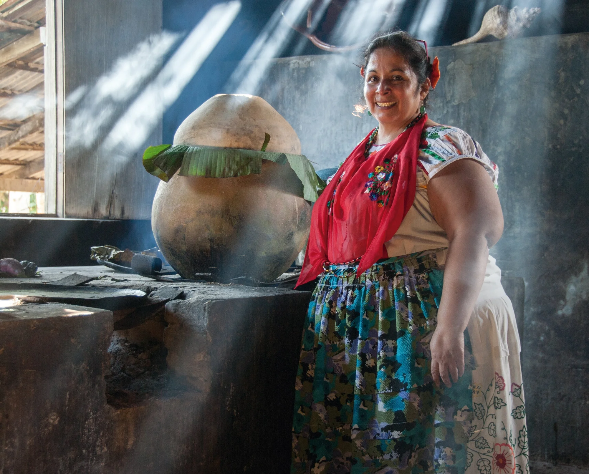 A woman stands in front of cooking materials in a traditional kitchen