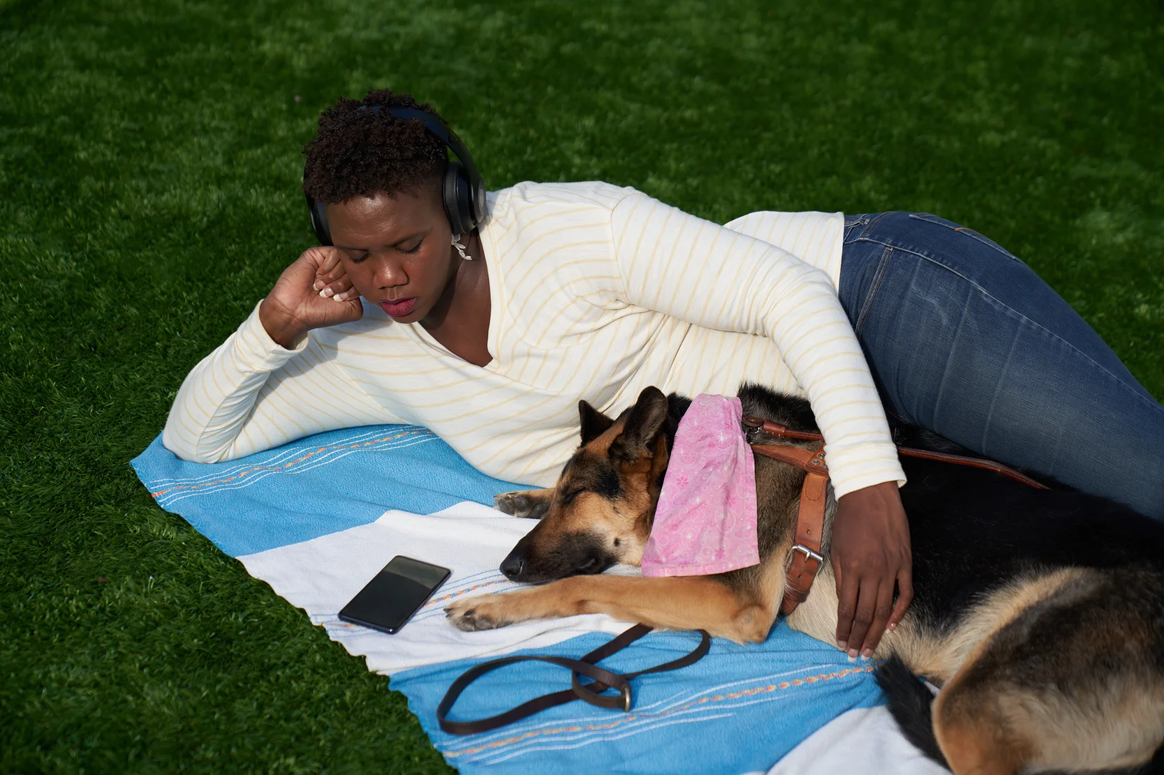 A woman who is blind or low vision lays on a blanket with her seeing eye dog, using her Android phone to use the TalkBack feature.