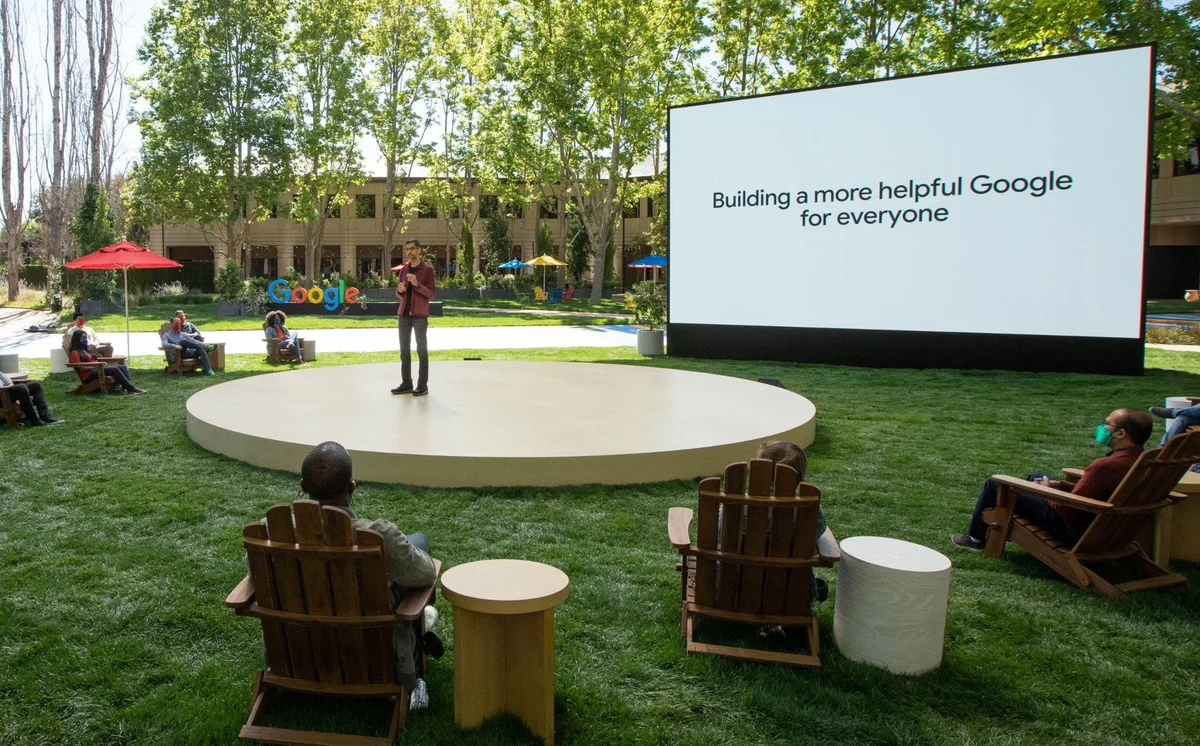 Sundar on stage at Google I/O 2021, with a display behind him reading "Building a more helpful Google for everyone"