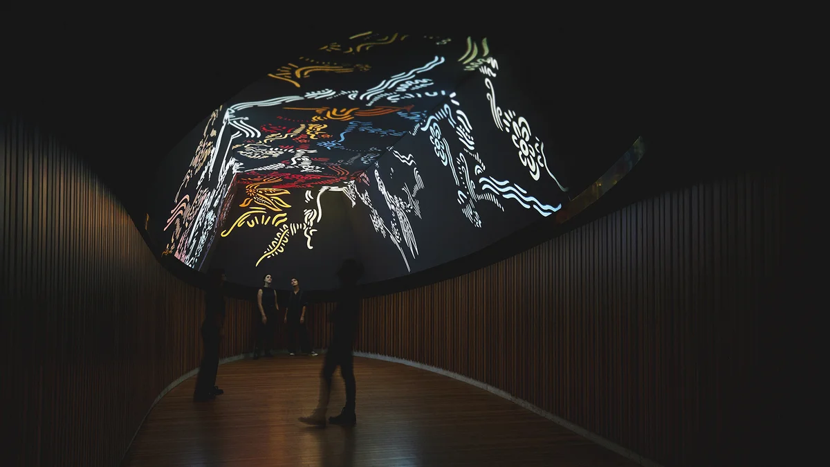 Three people stand inside a dark, cavernous space which features colourful artwork on the ceiling which they are peering up towards