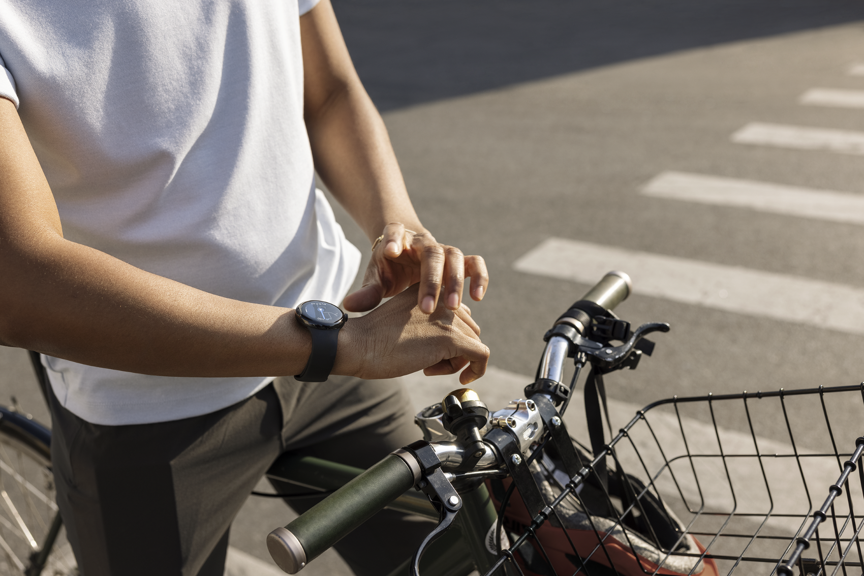 Ein Mann überprüft seine Google Pixel Watch, während er mit seinem Fahrrad an einem Zebrastreifen wartet.