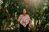 a woman from the Alabel Duche' collective stand in front of a three wearing traditional garment