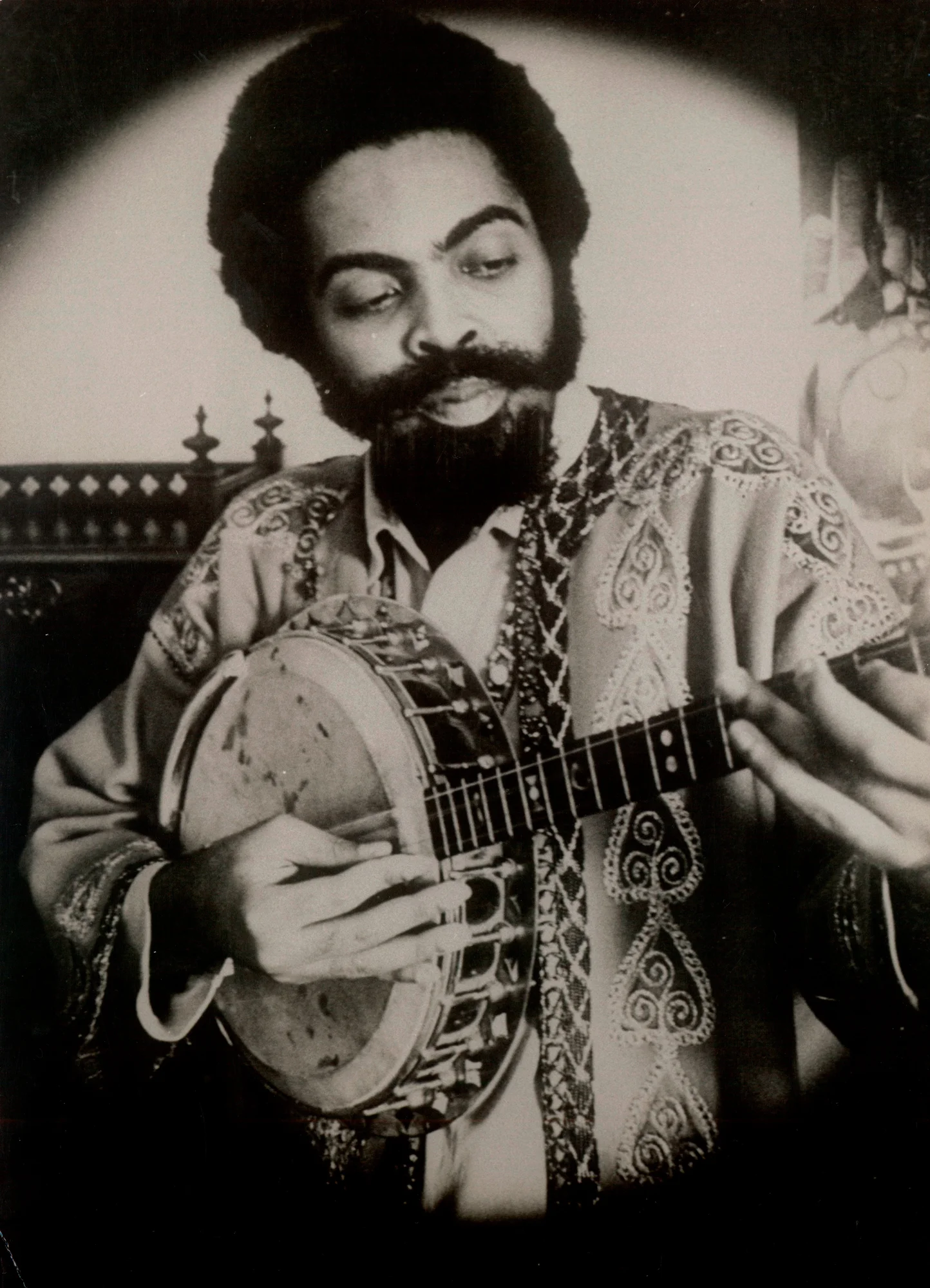 Foto em preto e branco de Gilberto Gil tocando um instrumento e vestindo roupas da época da Tropicália