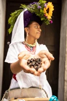 A woman with a flower on her head, hands outstretched holding coffee beans