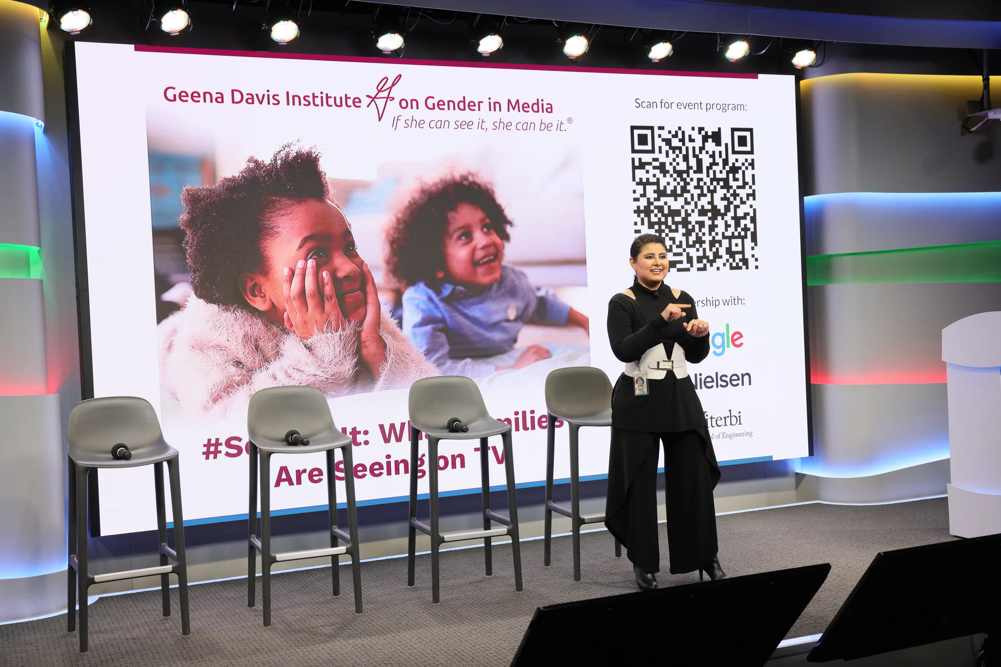 Person standing in front of a wall-sized presentation screen. Presentation referencing the GDI report