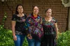 Enedina Lara, Julia Hernández y Erika Reynoso posan para una foto con sus propias creaciones de prendas bordadas de colores