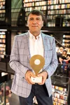 Bookshop owner Ton Harmes stands in front of bookcases holding his Golden Pin trophy from Google