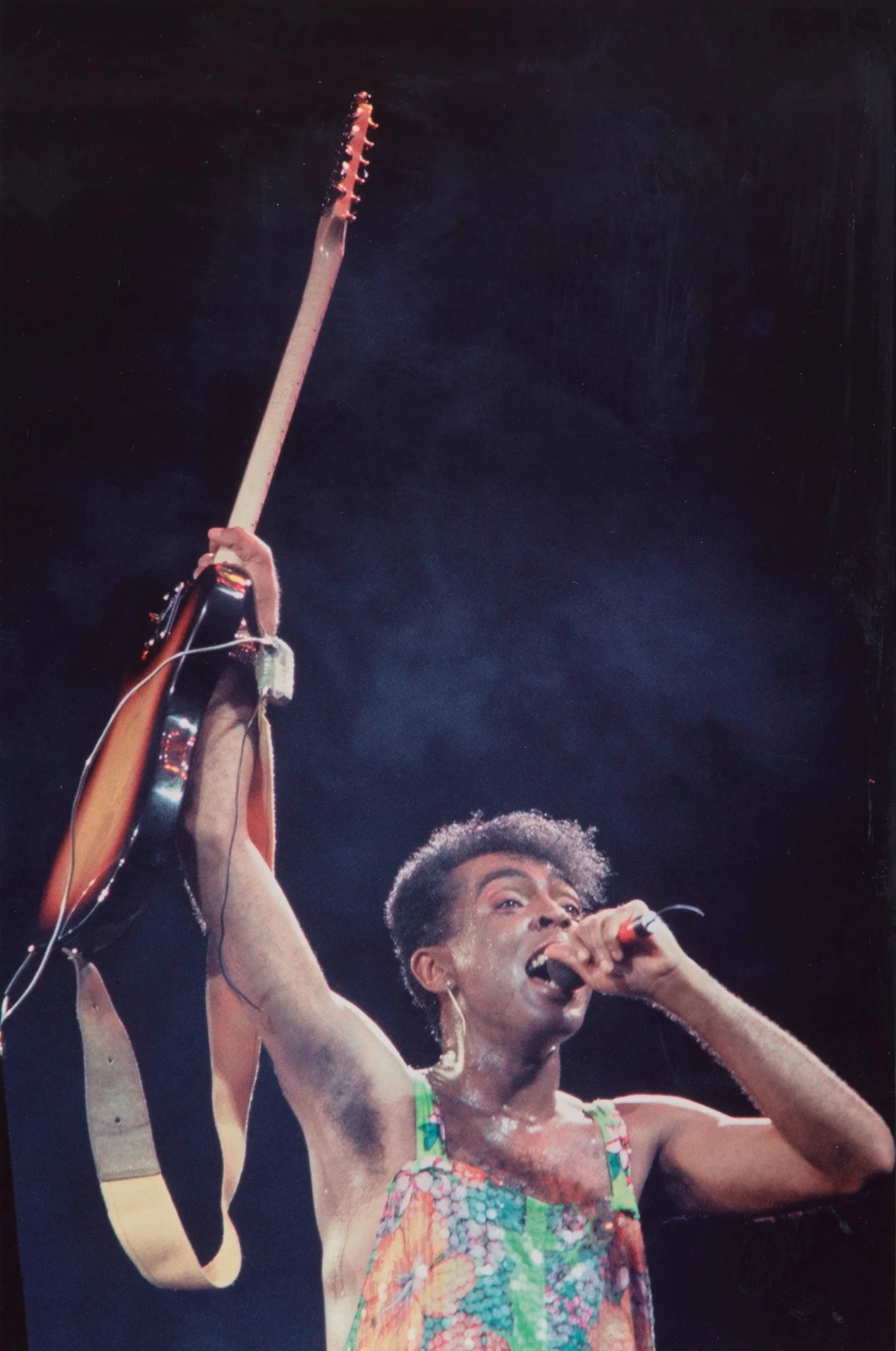 Gilberto Gil holding up his guitar and singing into the icrophone
