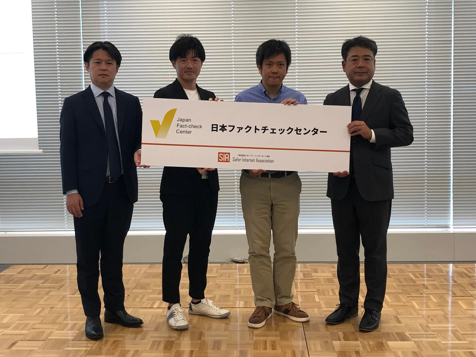 Four men stand holding a placard that says “Japan Fact-check Center”