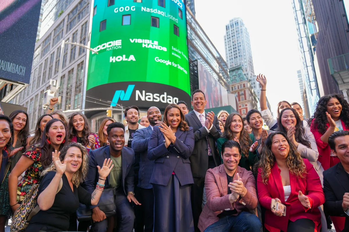 A large group of people stand smiling at the camera in front of the NASDAQ building in Times Square, which is brightly light with a sign reading "Google for Startups Latino Founders Fund."