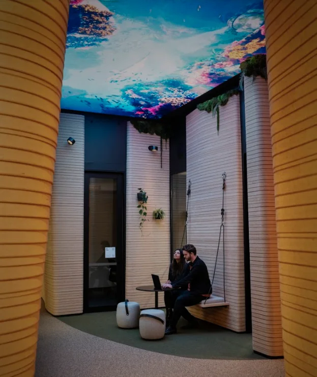 A photo of the colourful 'digital ceiling' in Google's new Auckland office, with a Googler working on a laptop at a table underneath the ceiling.