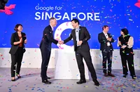 Two people shaking hands on stage, with confetti in the air. The wall behind them reads: Google for Singapore.