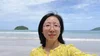 Jenny takes a selfie on a beach with the ocean and two small islands behind her.