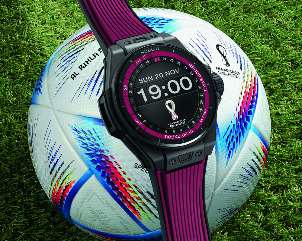FIFA World Cup themed soccer ball with Hublot’s World Cup edition smartwatch laying across on top showing the time and the World Cup banner.