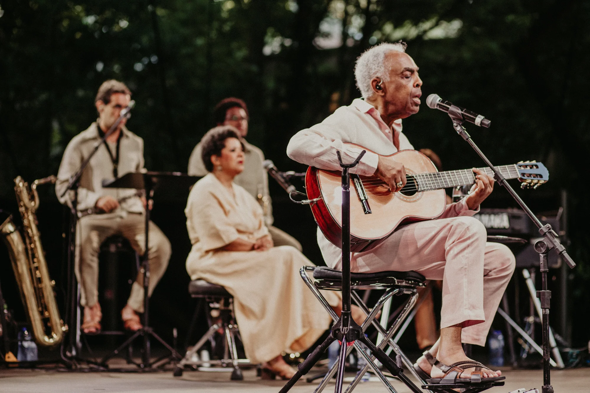 Gilberto Gil playing the guitar on stage with his band behind him