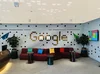 Une zone de réception dans le bureau de Google à Dubaï avec un canapé rouge, trois tables d'appoint noires et le mot Google écrit en carreaux sur un mur ondulé.