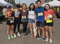 Six Googlers smiling at the camera outside on the street. All of them are wearing exercise gear, with some wearing a running number attached to their shirts. Three of the Googlers are wearing red and gold medals with red ribbons.