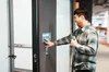 A person with a cane puts their hand on a braille sign outside of a room.