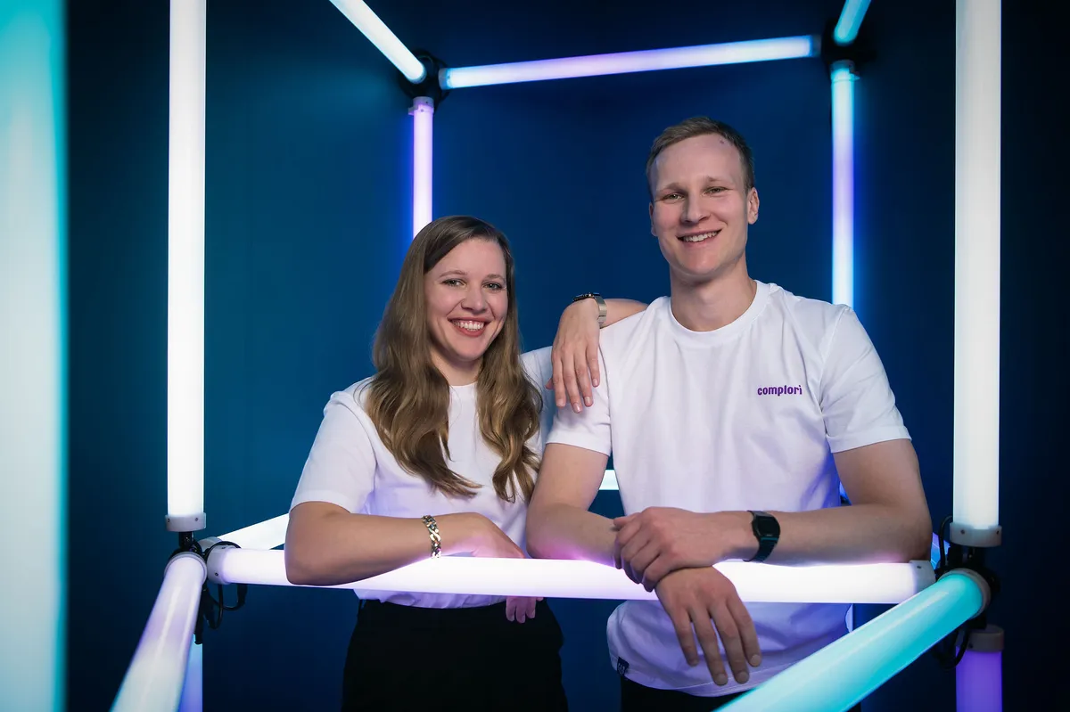 A woman wearing a white shirt and a man wearing a white shirt stand side by side in a brightly lit room.