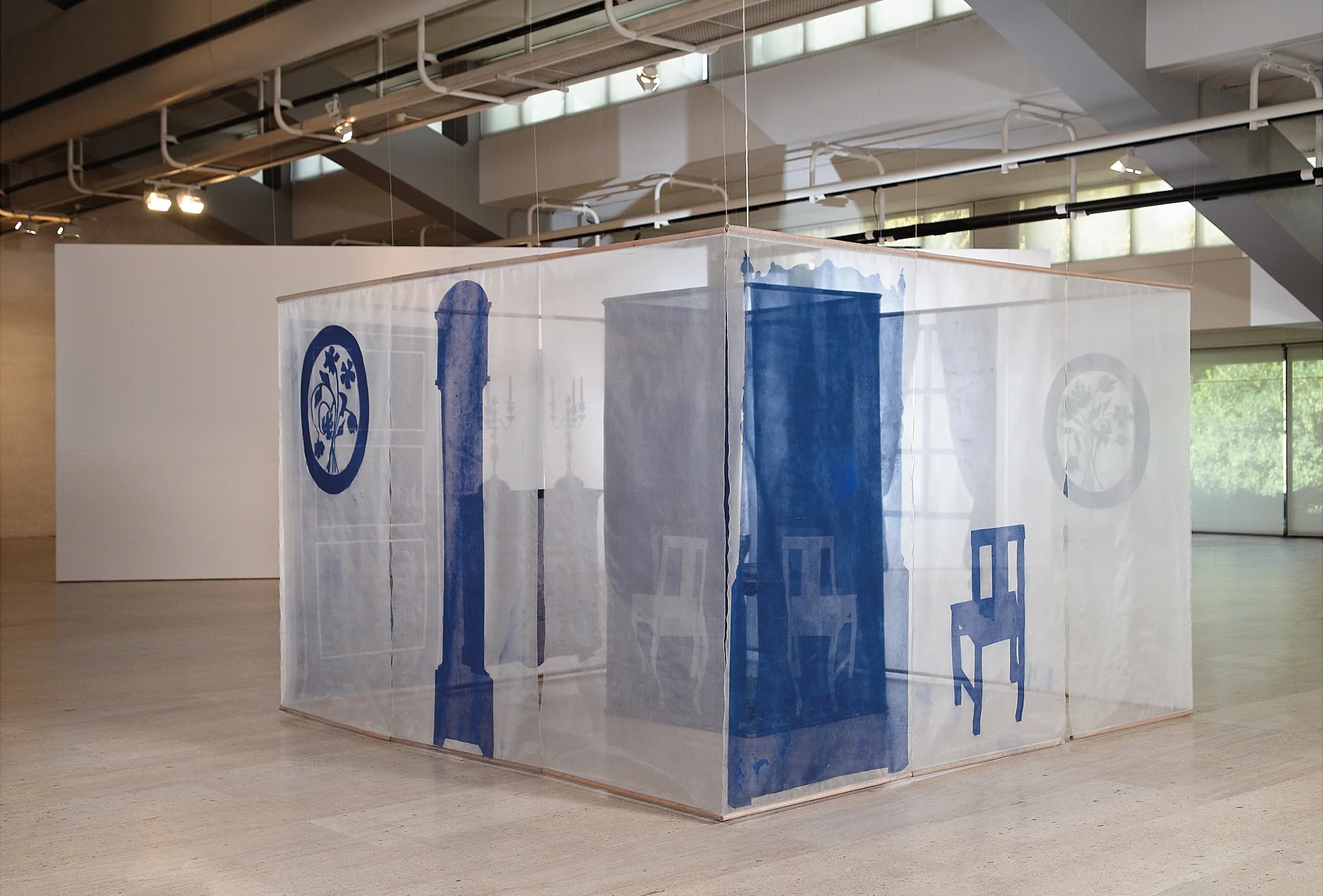 An exhibit featuring white fabric hanging from the ceiling with chairs and other furniture painted on it in blue.