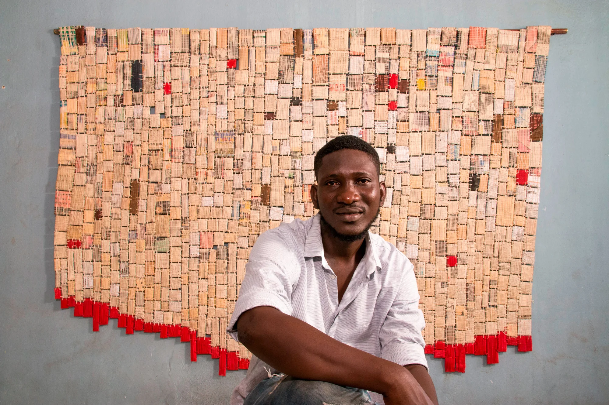 Ange Dakou in front of one of his woven gris gris pieces of art.
