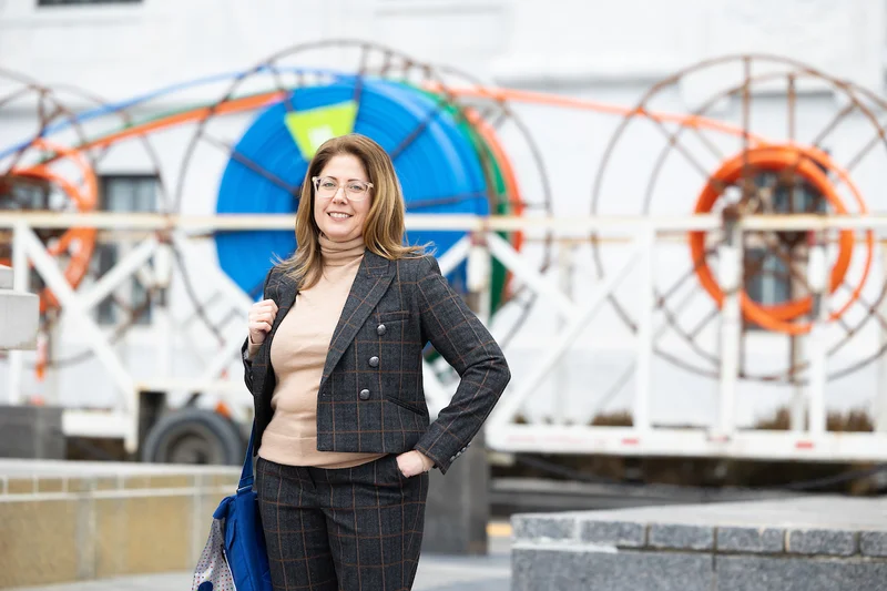 Headshot of Angela wearing a plaid suit and standing in front of large cables.