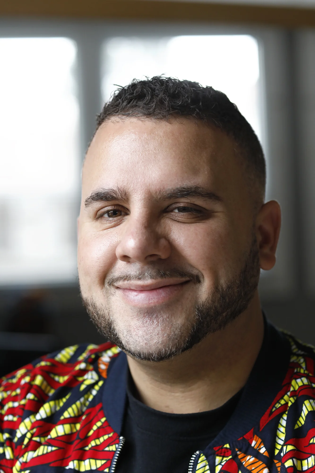 Close-up photo of Anthony smiling at the camera and wearing a red and green jacket.