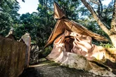 A uniquely shaped structure with a triangular bamboo roof in a forest