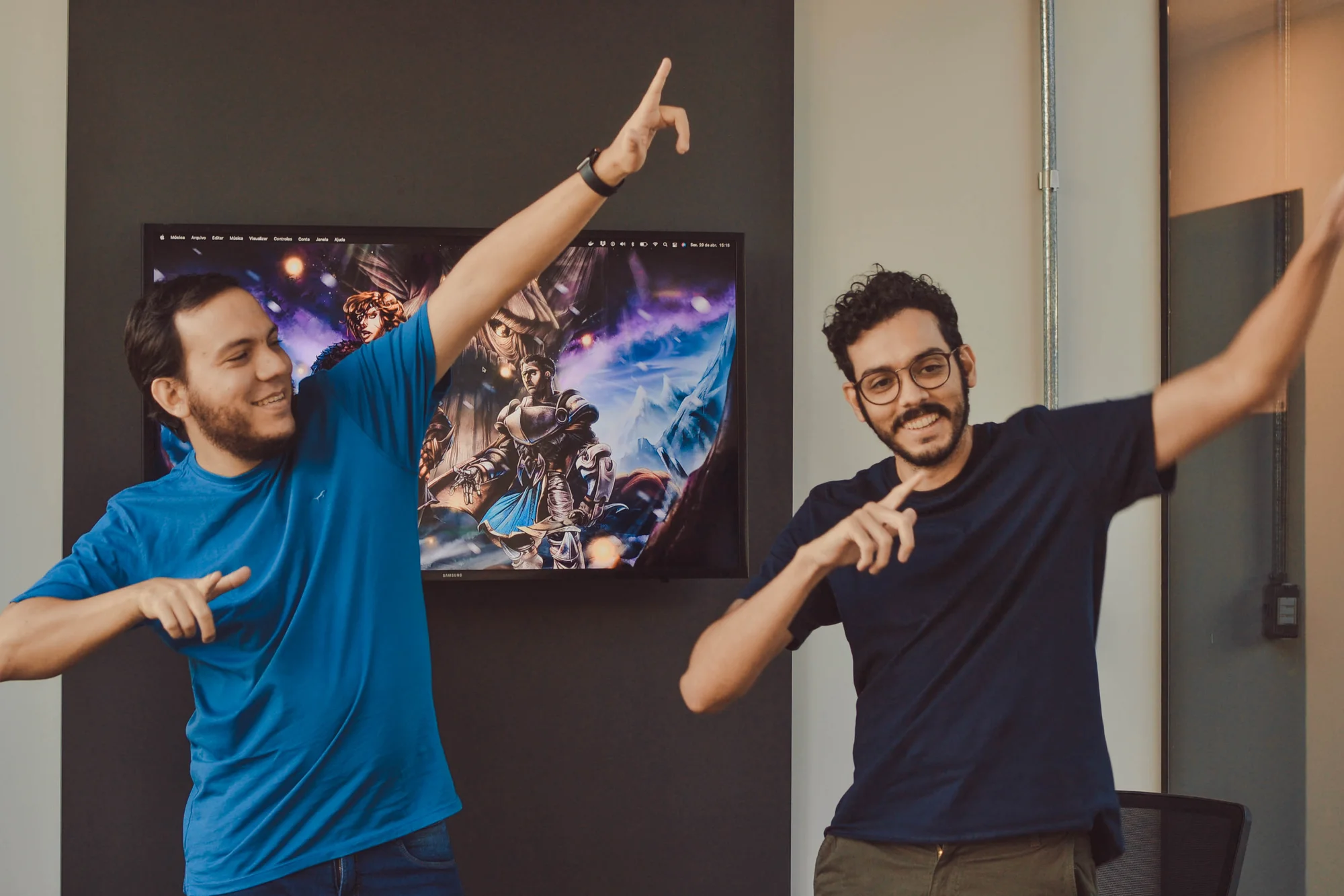 Two people wearing t-shirts smile and point to the right.