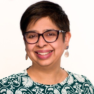 This is a photo of a woman smiling wearing glasses in front of a light background.