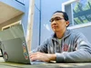 A man in a sweatshirt looking at a laptop computer.