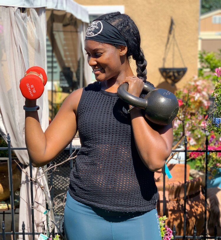 Brittany holds a hand weight and kettlebell wearing black top and blue pants