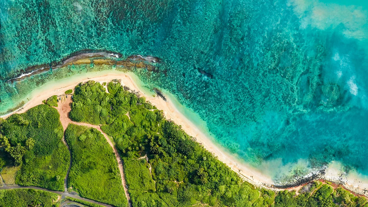 Aerial image of the coast line showing greenery set against sandy beaches and blue ocean waters.