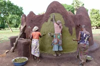 A group of 3 young women restoring a mud structure, layering it with green material.