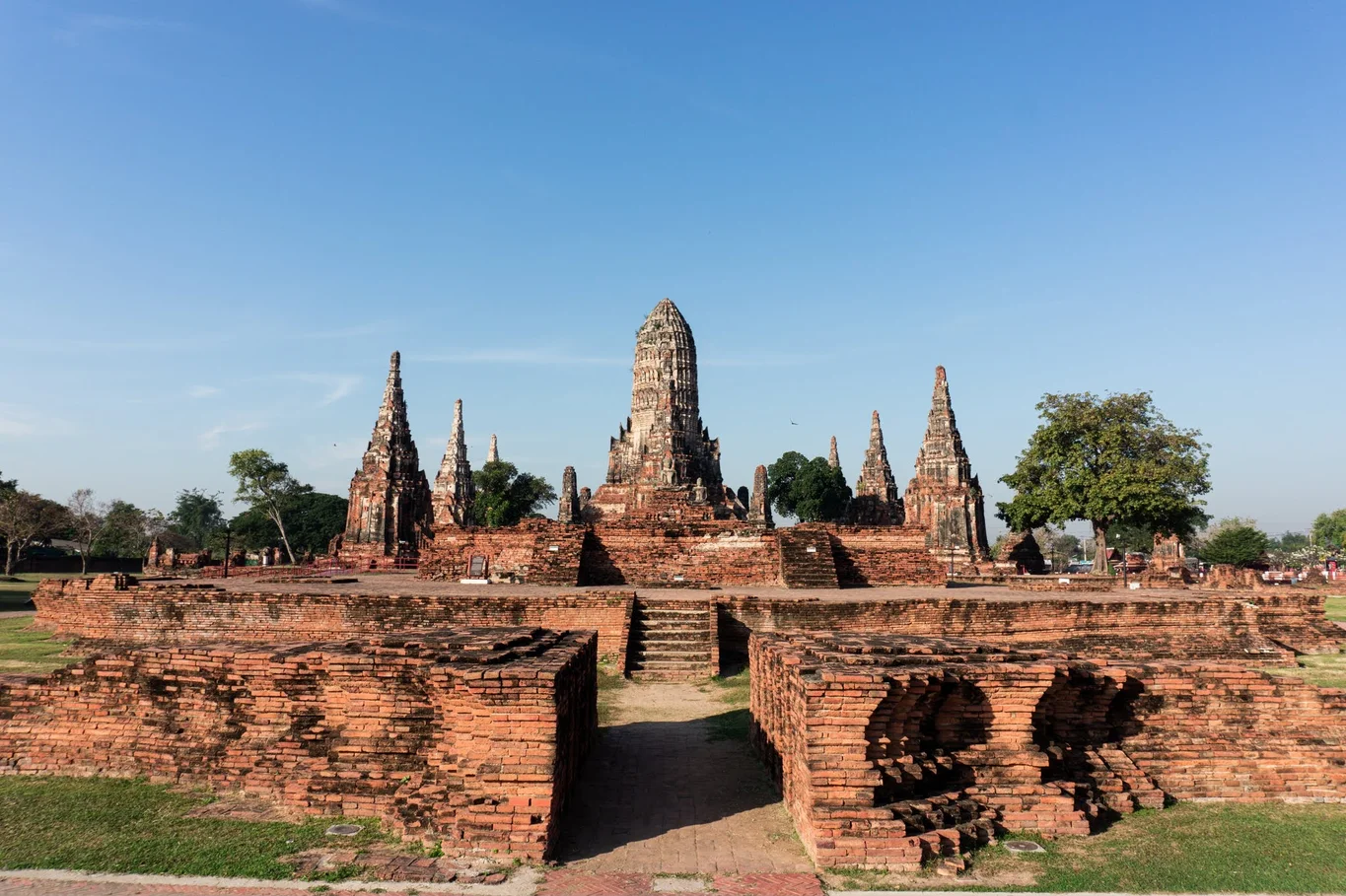 A landscape view o f symmetric earth-colored temples with pointed tops, against a blue sky and some greenery.