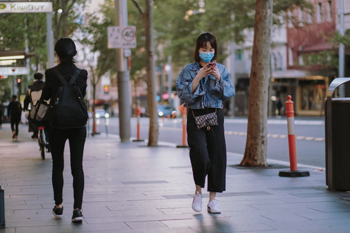 Frau mit Maske läuft auf einer Straße mit einem Smartphone in der Hand