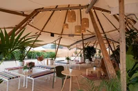 A workspace set up under a large canvas tent, with many tables and chairs, as well as plants and other decorations