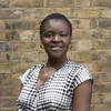 A Black woman with short brown hair and wearing a black and white patterned shirt smiles at the camera.