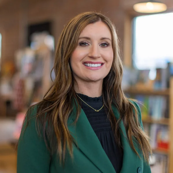 A woman wearing a green blazer smiles directly at the camera.