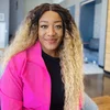 A Black woman with long blonde hair and wearing a pink blazer sits facing the camera.