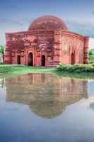 One dome mosque in red brick and the damaging effects of salinity, reflecting in the water around it.