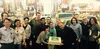 A group of people stand against a backdrop of Times Square. In the middle, two people hold a cake with the Google Classroom logo on top.