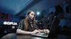 A woman at a laptop, sitting in a studio next to a large microphone.