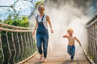 A women and child crossing a bridge through a moisture cloud