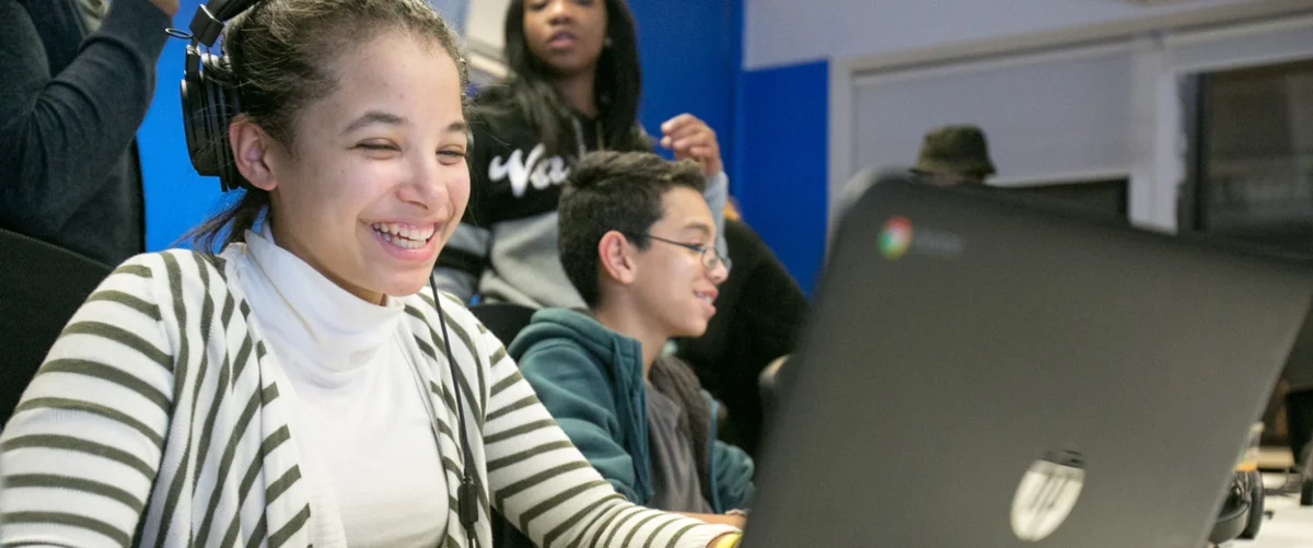 Two students participating in Google’s Code Next program. They are sitting in front of open laptops and smiling.