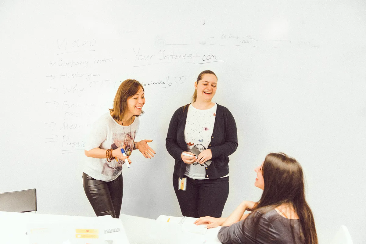 A photo of three female founders smiling and working on a whiteboard