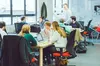 A photo of several females and males working, talking and smiling at desks with laptops