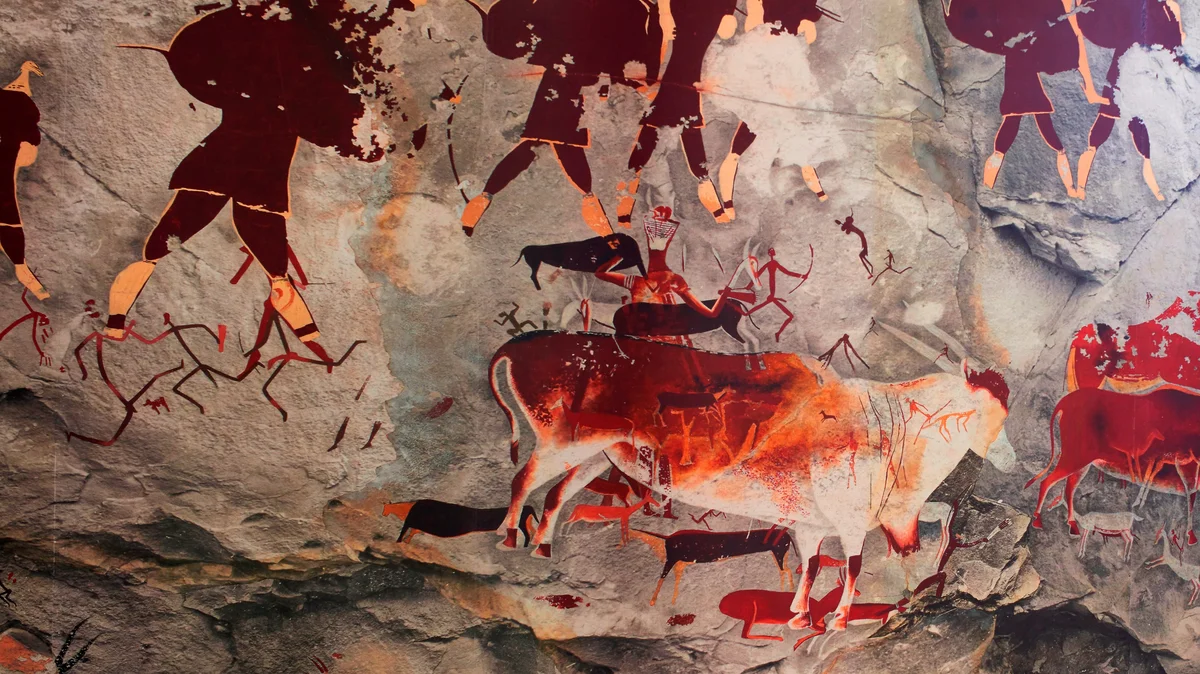 this image depicts painted images in shades of dark red, sand and brown and orange. The images show elands, half human and animal forms (known as therianthropes) and hunters holding bow and arrows.